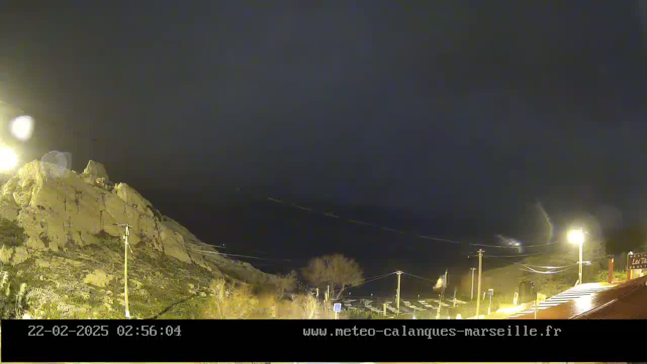 A nighttime view of a rocky hillside overlooking a dark body of water under a cloudy sky.