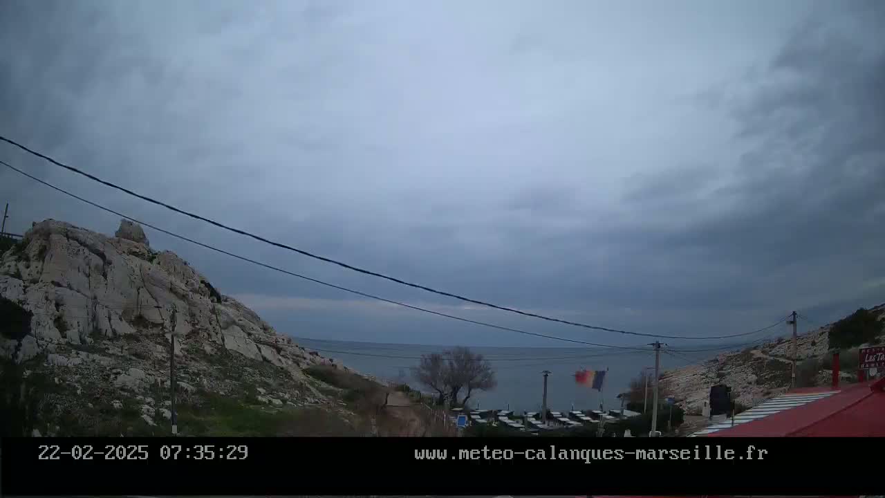 A rocky hillside overlooks a calm sea under an overcast sky.