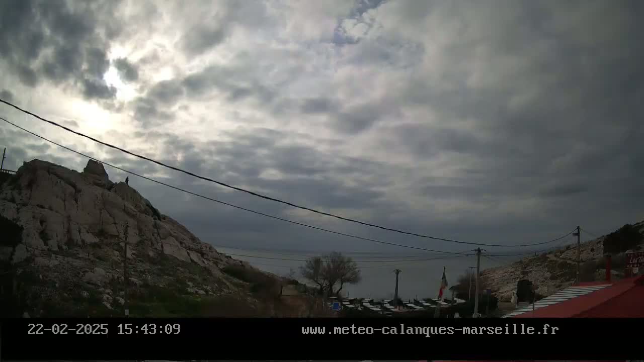 A rocky hillside overlooks a calm body of water under a mostly cloudy sky.