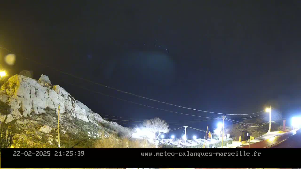 A nighttime view of a rocky hillside under a dark, clear sky with a few faint lights visible in the distance.