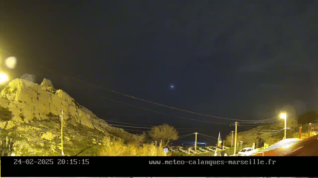 A nighttime view shows a rocky hillside illuminated by artificial lights under a dark, clear sky with a single bright star visible.