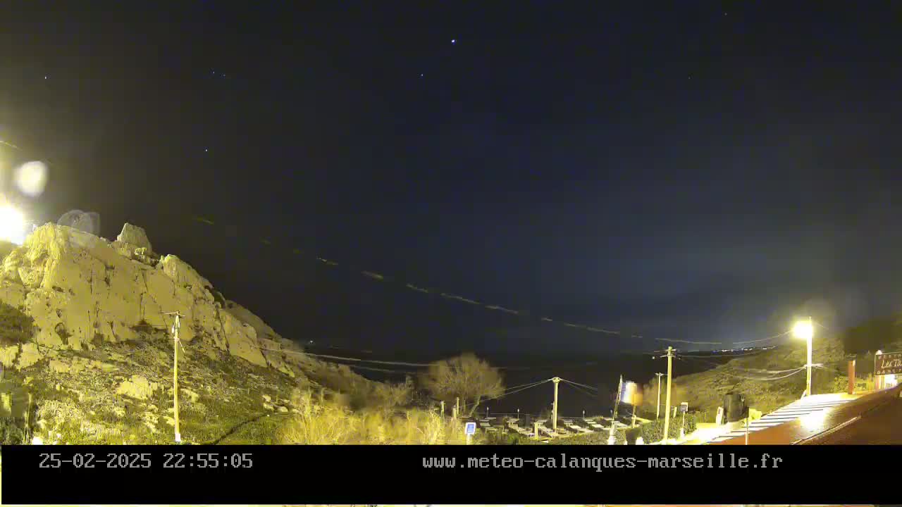 A nighttime view of a rocky hillside overlooking a calm body of water under a clear, starlit sky.