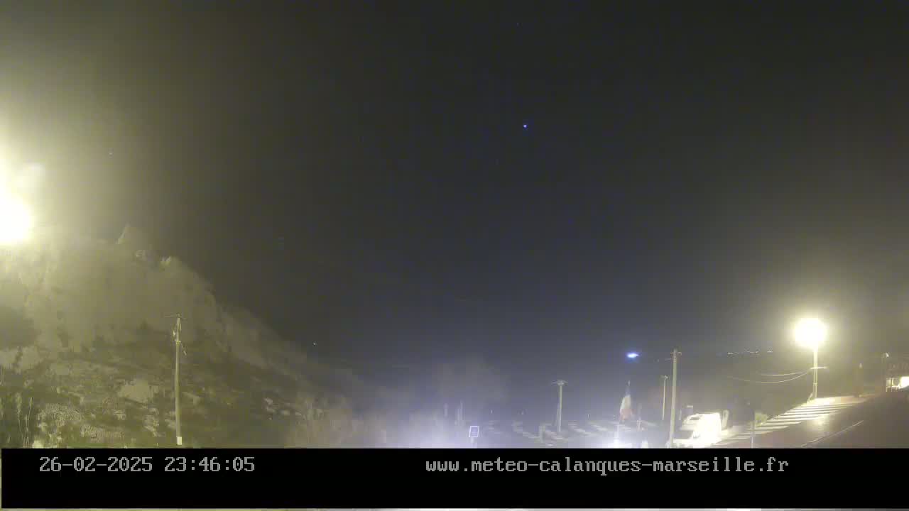 A nighttime, hazy scene shows a roadway with some vehicles, illuminated by streetlights, next to a large, light-colored hill or cliff.