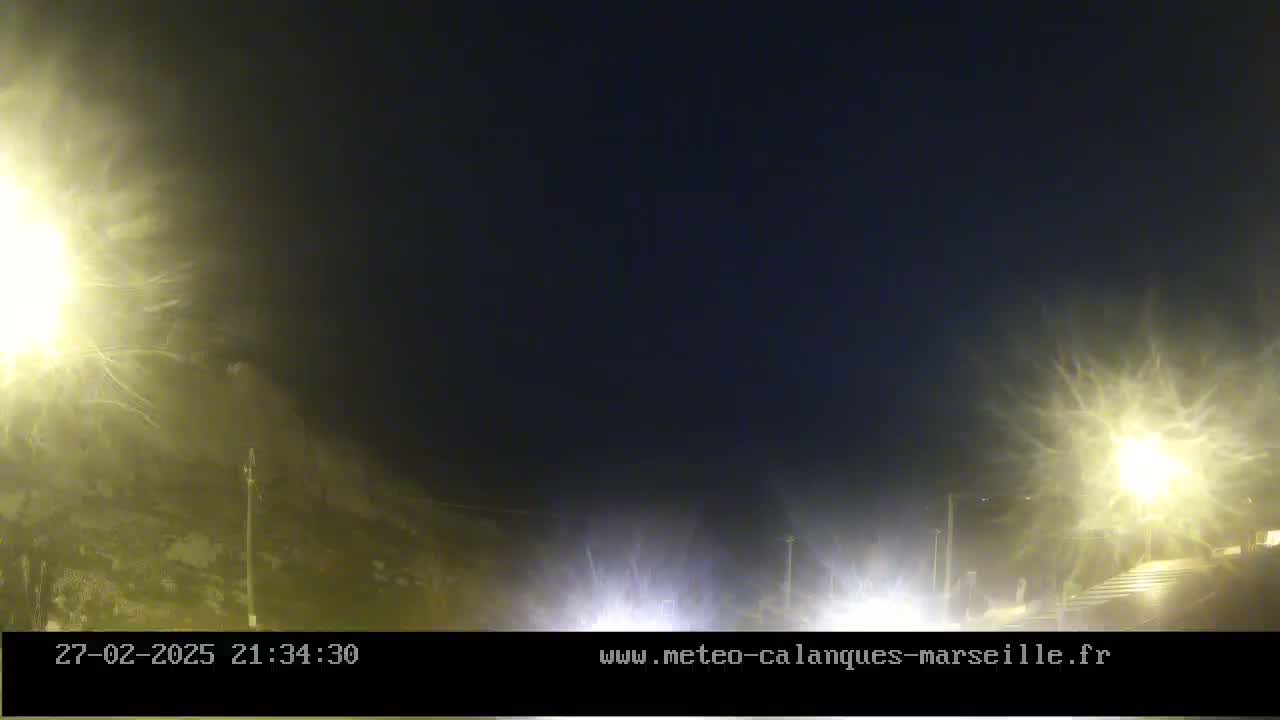 A nighttime, hazy scene shows a hill under bright streetlights with blurry headlights of vehicles in the foreground.
