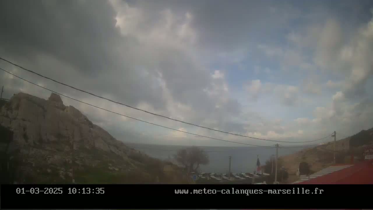 A partly cloudy day overlooks a rocky hillside and calm body of water, with power lines running across the scene.