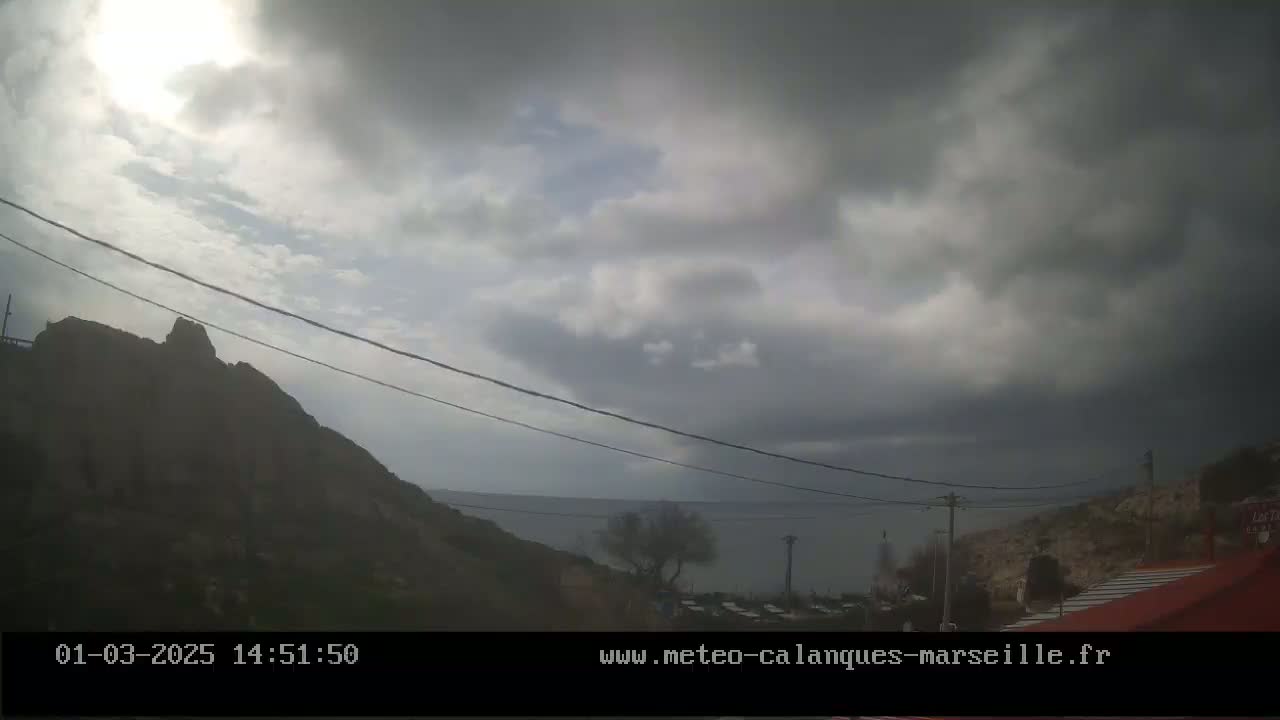 A mostly cloudy day shows a rocky hillside overlooking a calm body of water under a gray sky.