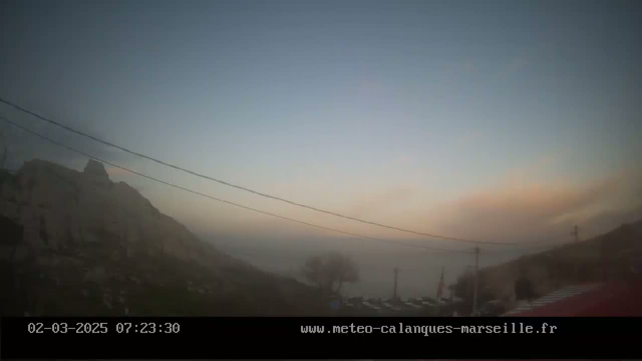 A hazy, dawn-lit landscape shows a rocky hill shrouded in fog, with power lines stretching across the scene, and a parking area visible in the foreground.