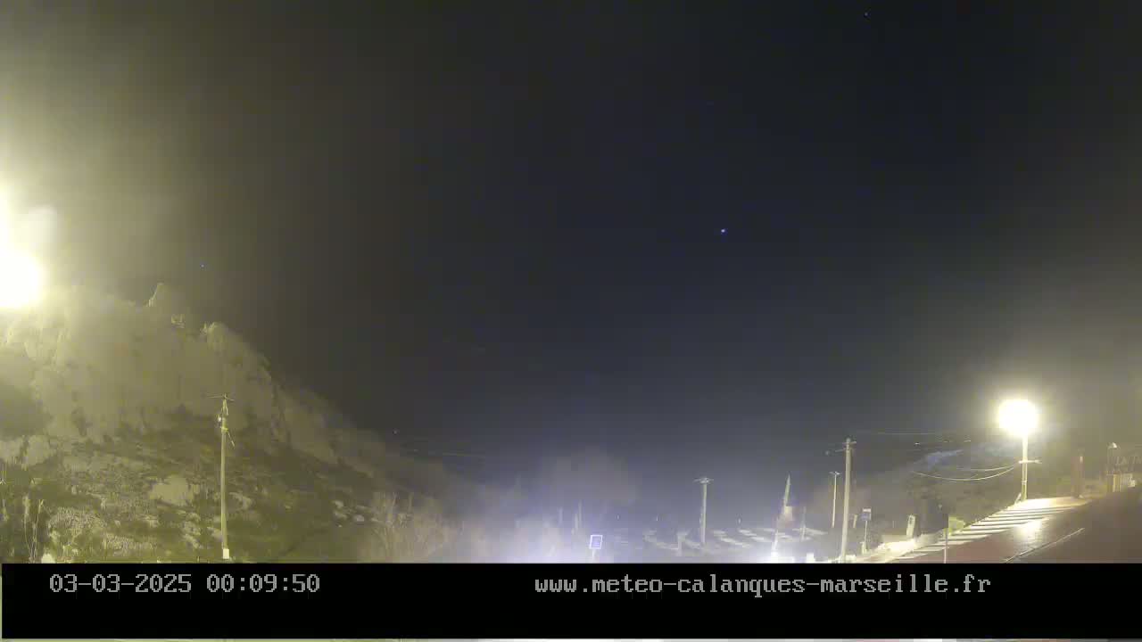 A nighttime view of a rocky hillside illuminated by streetlights under a mostly clear, dark sky.