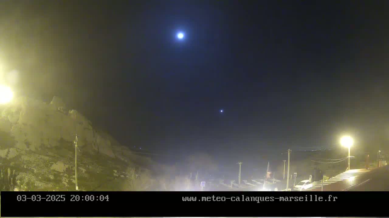 A nighttime view shows a moonlit sky above a rocky hillside and a hazy parking lot with a few vehicles.