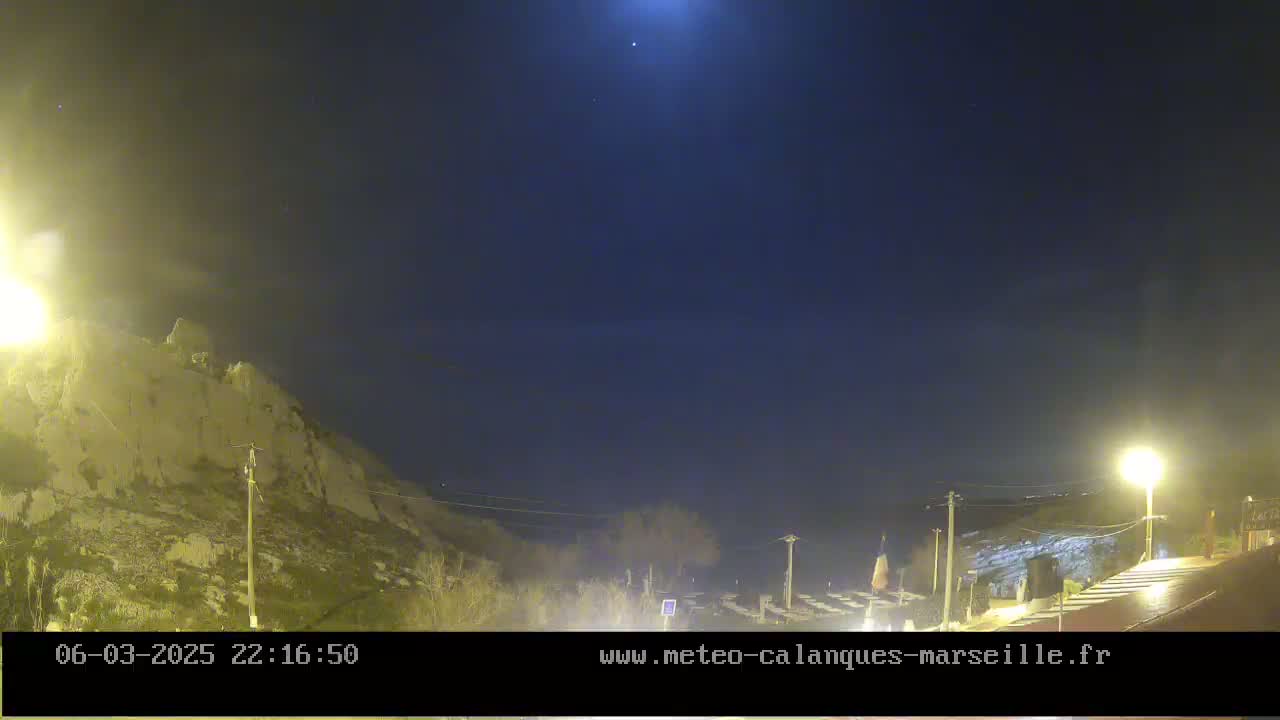 A nighttime, outdoor scene shows a bright moon in a dark sky above a rocky hillside and a sparsely lit roadway.