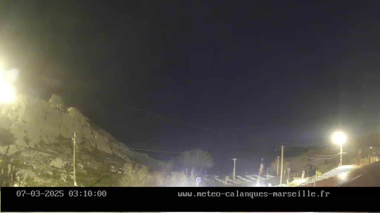 A nighttime view of a rocky hillside illuminated by streetlights under a dark, clear sky.