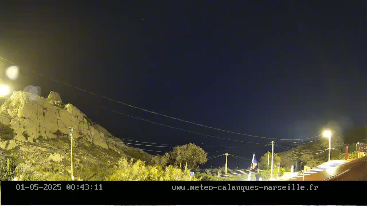 A nighttime view shows a rocky hillside under a clear, dark sky dotted with a few stars, illuminated by streetlights.