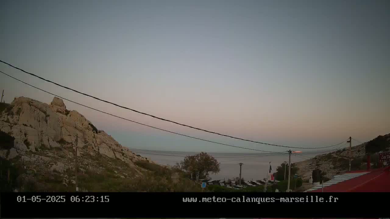 A rocky hillside overlooks a calm sea under a pale pink and gray twilight sky.
