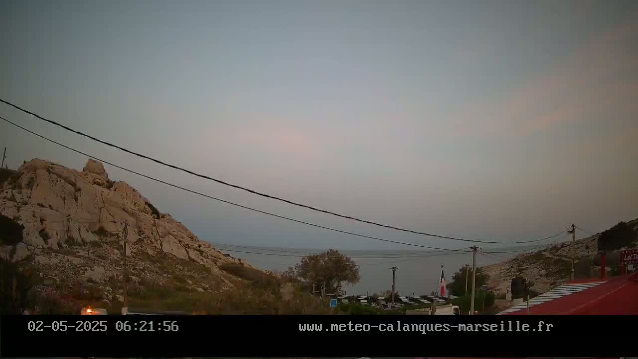 A rocky hillside overlooks a calm sea under a hazy, pale sky at dusk.