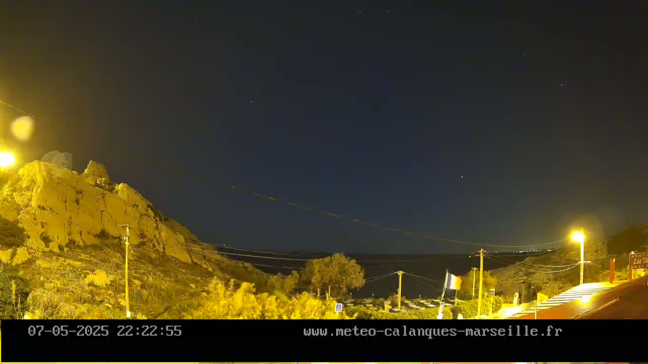 A nighttime view of a rocky hillside overlooking a calm body of water under a clear, starlit sky.