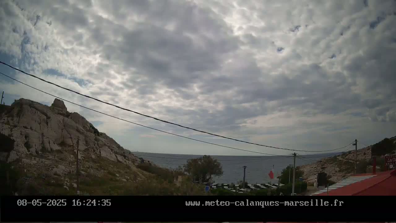 A rocky hillside overlooks a calm sea under a mostly cloudy sky.