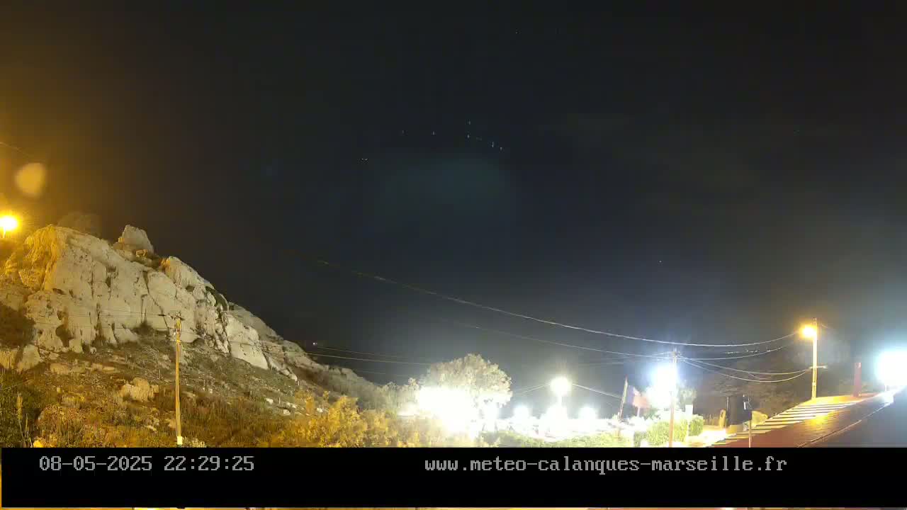 A rocky hillside illuminated by artificial light is visible under a clear, dark night sky.