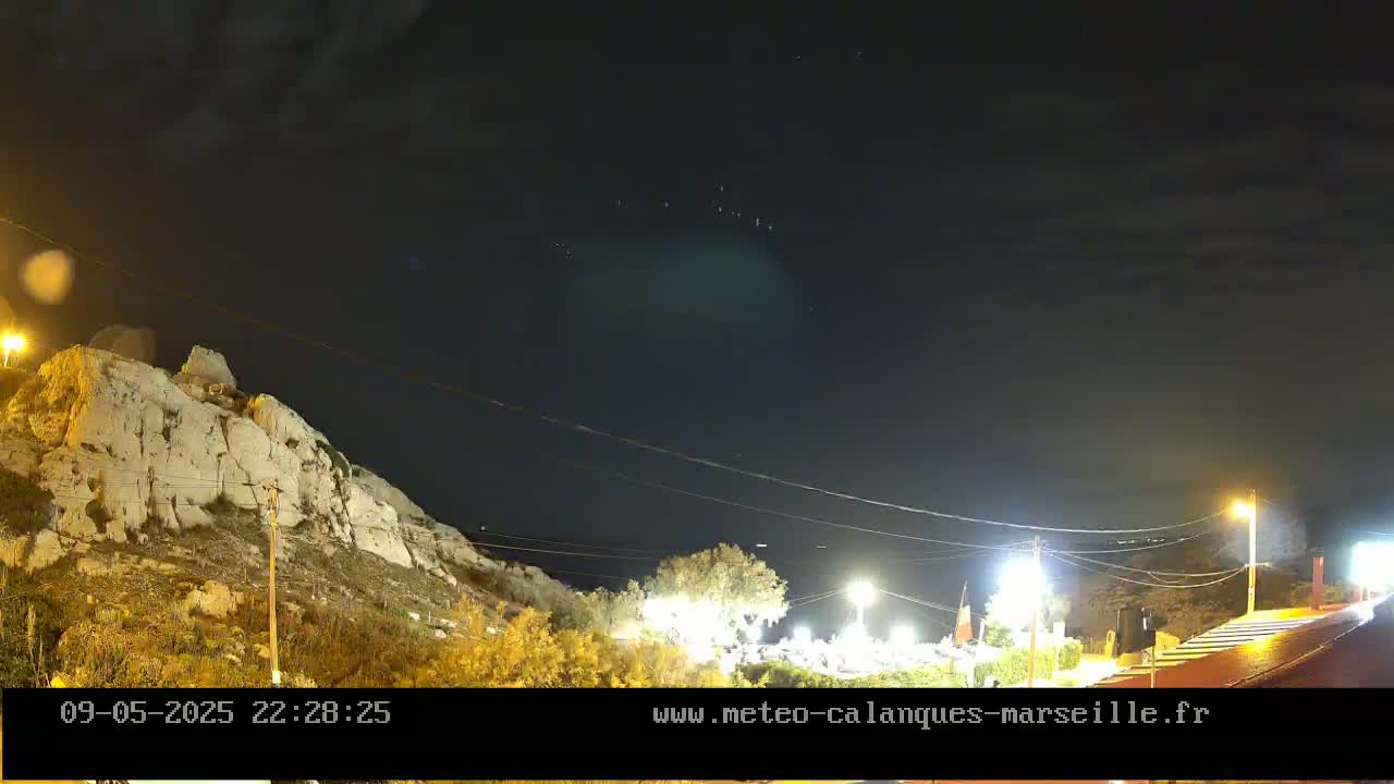 A nighttime view of a rocky hillside illuminated by streetlights, with a mostly clear sky showing a few faint lights.