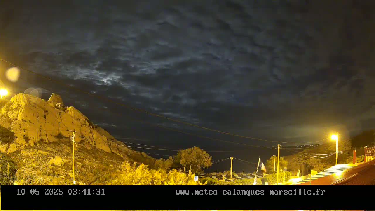A nighttime view of a rocky hillside illuminated by streetlights under a cloudy sky.