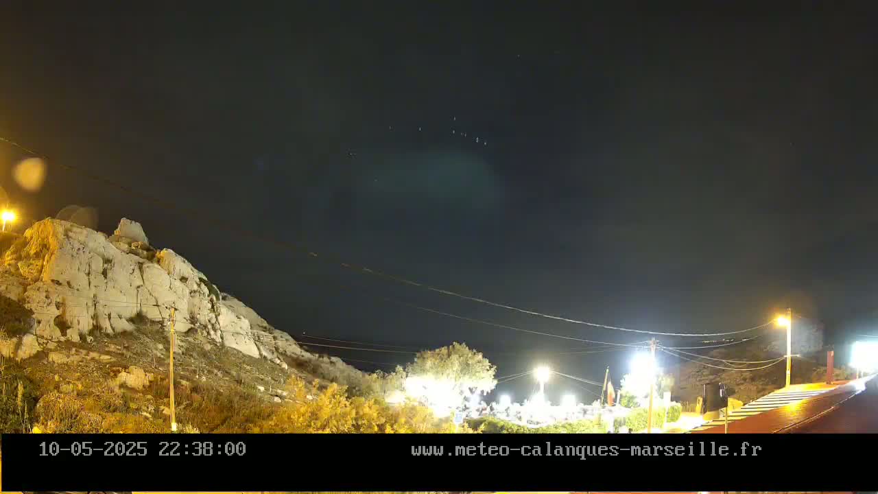 A nighttime view of a rocky hillside illuminated by artificial lights, with a clear sky showing a few distant lights.