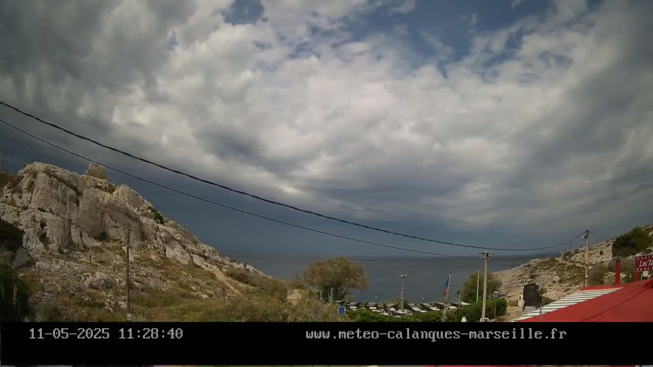 A rocky hillside overlooking a calm sea under a partly cloudy sky.