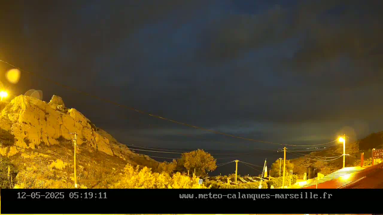 A nighttime view of a rocky hillside overlooking a dark body of water under a mostly cloudy sky.