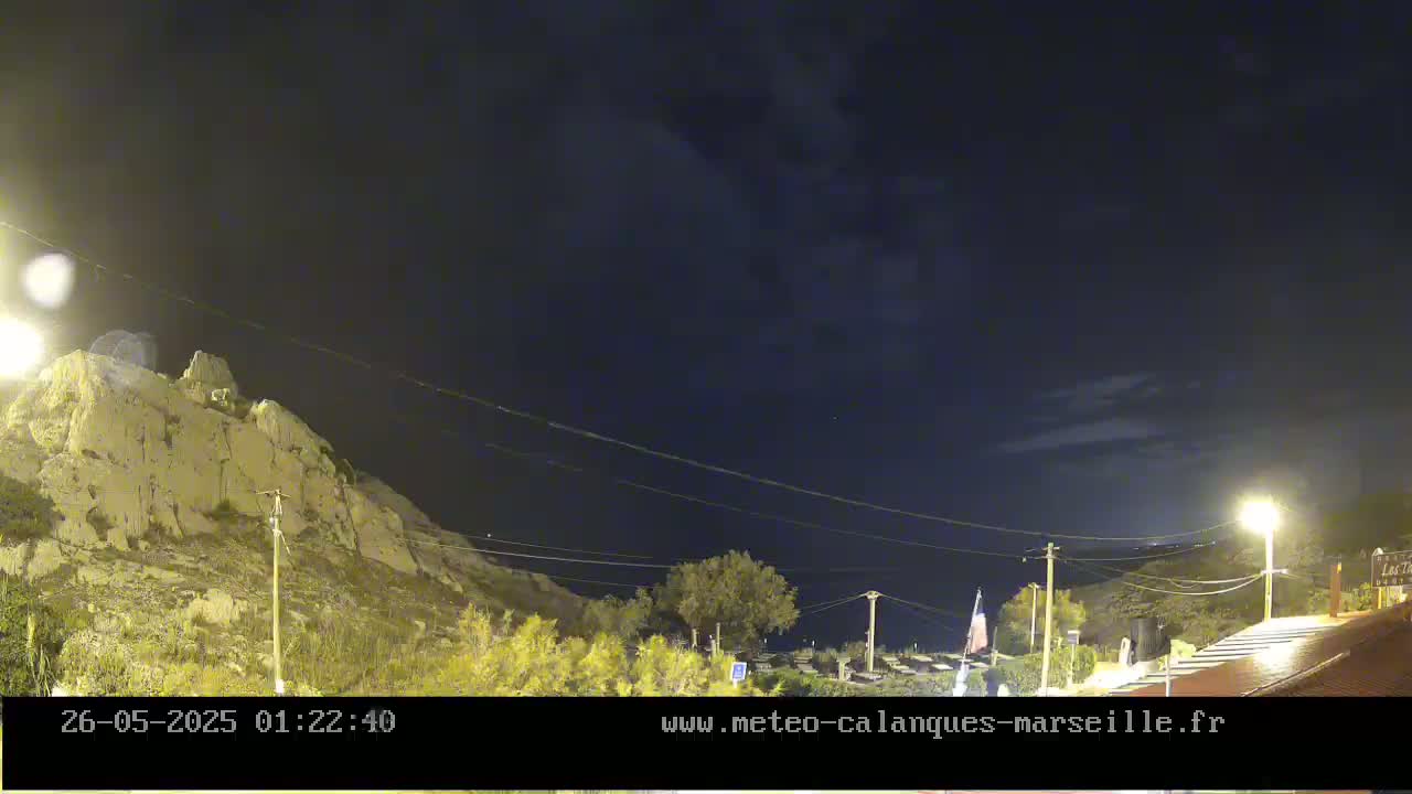 A nighttime view of a rocky hillside illuminated by streetlights under a mostly clear, dark sky.