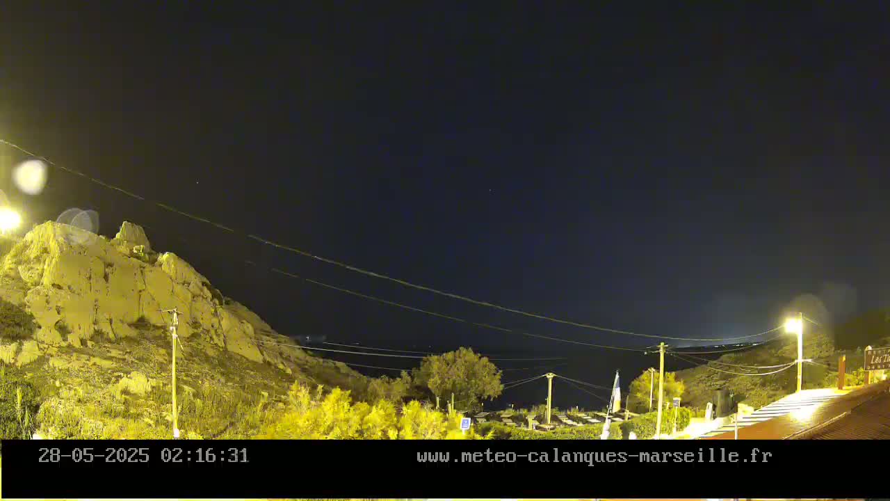 A nighttime view of a rocky hillside overlooking a calm body of water under a clear, dark sky.