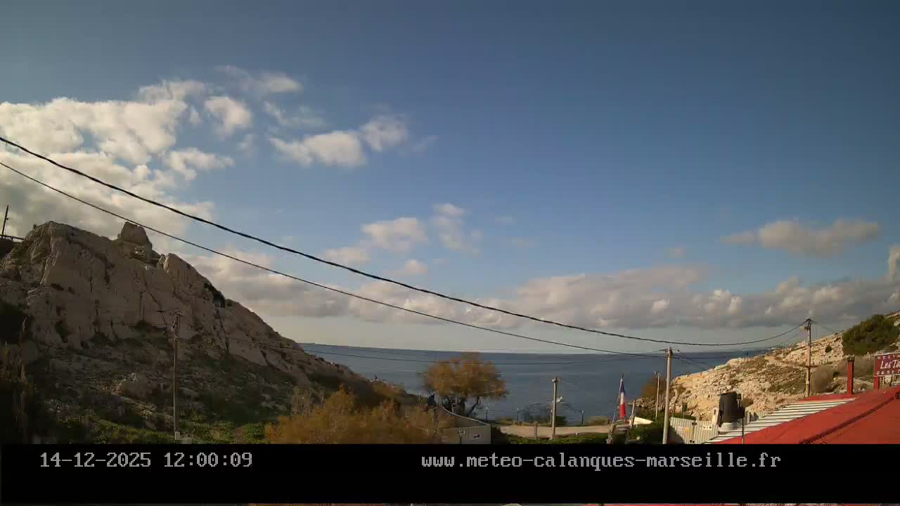A rocky, pale cliff dominates the left side of a nighttime landscape under an overcast sky, with scattered artificial lights illuminating sparse vegetation and a path on the right.