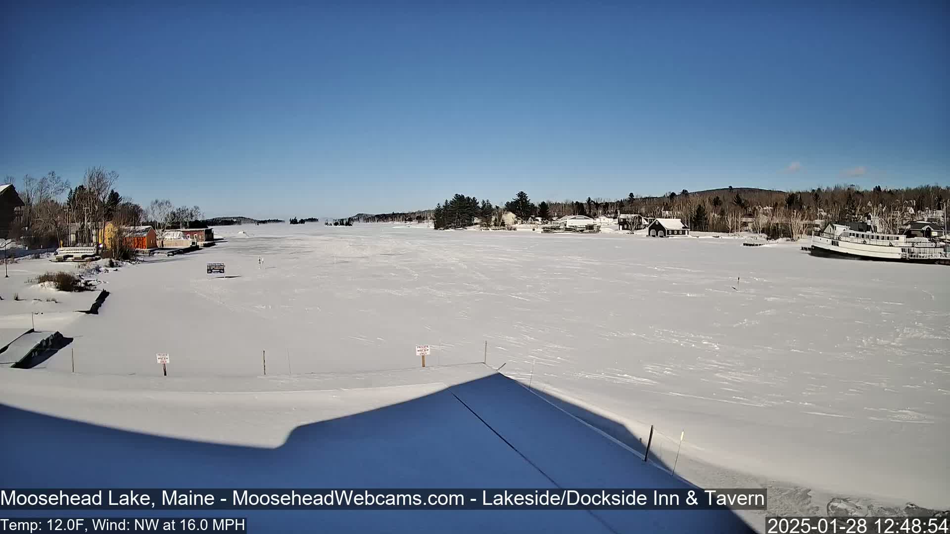 A frozen lake is visible, under a clear blue sky, with buildings and trees lining the shore in the distance.
