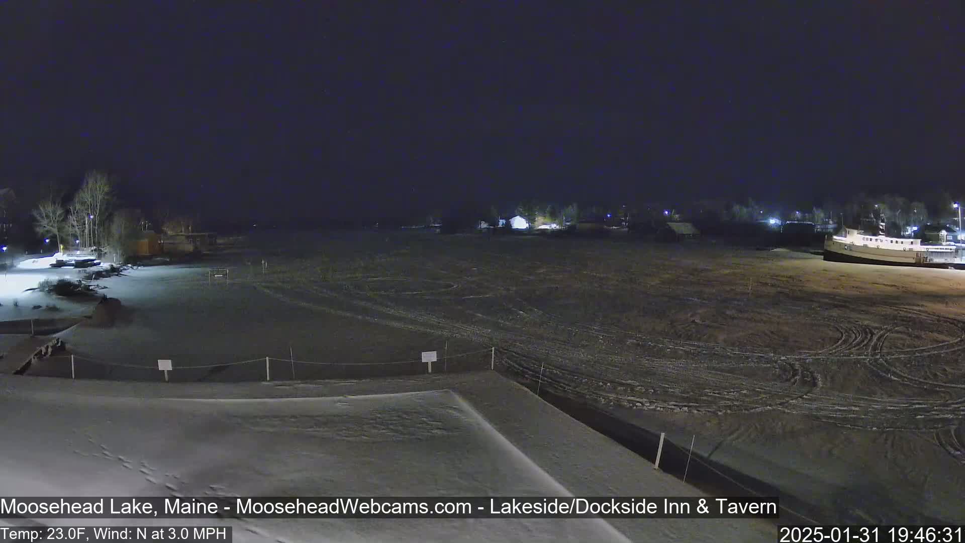 A snow-covered lakeside area at night, under a dark sky with a north wind at 3.0 mph and a temperature of 23 degrees Fahrenheit.