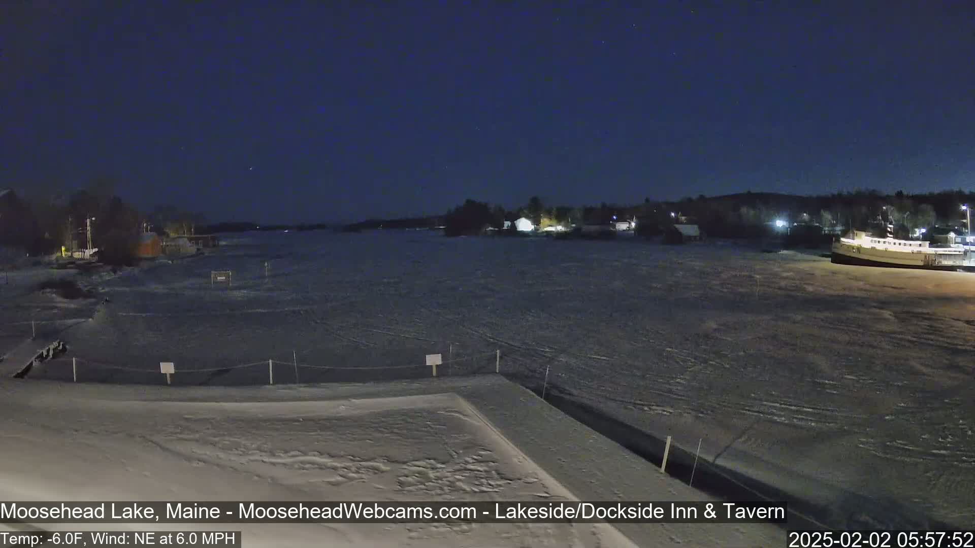 A snow-covered dock overlooks a partially frozen lake at night under a dark, clear sky.