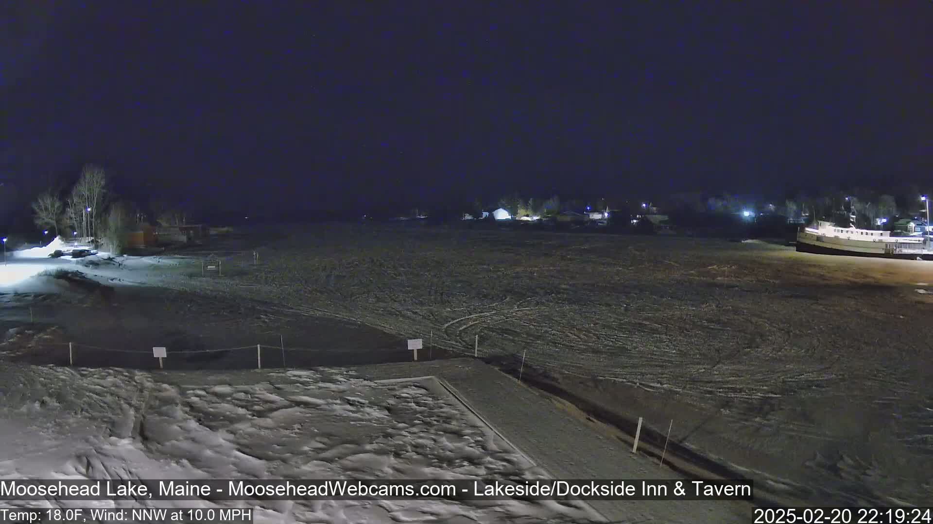A nighttime view of a snow-covered shoreline with a body of water partially frozen under a dark sky, with a north-northwest wind at 10 mph and a temperature of 18°F.
