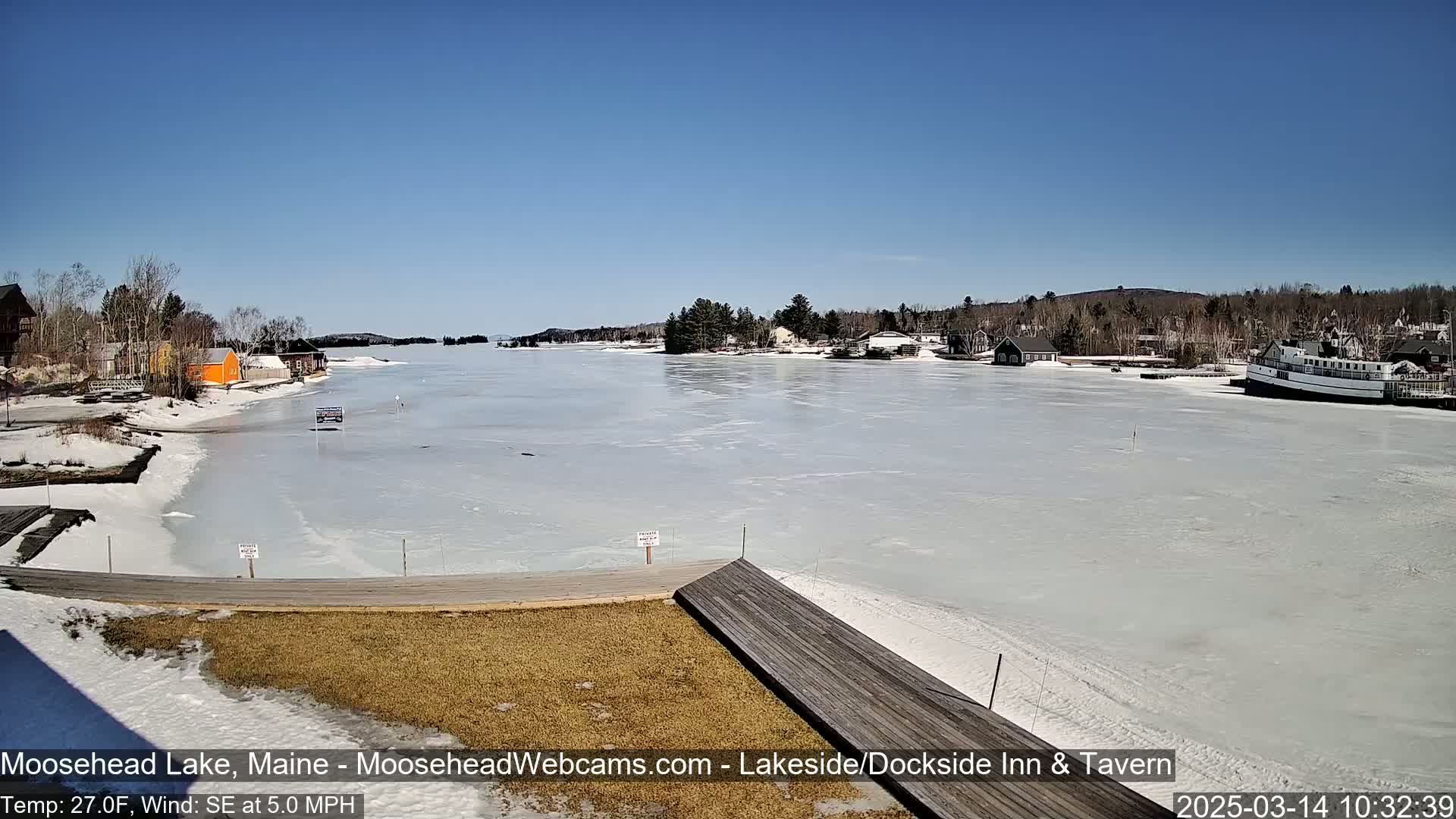 A mostly frozen lake is seen from a lakeside dock on a sunny day with a light southeast wind.