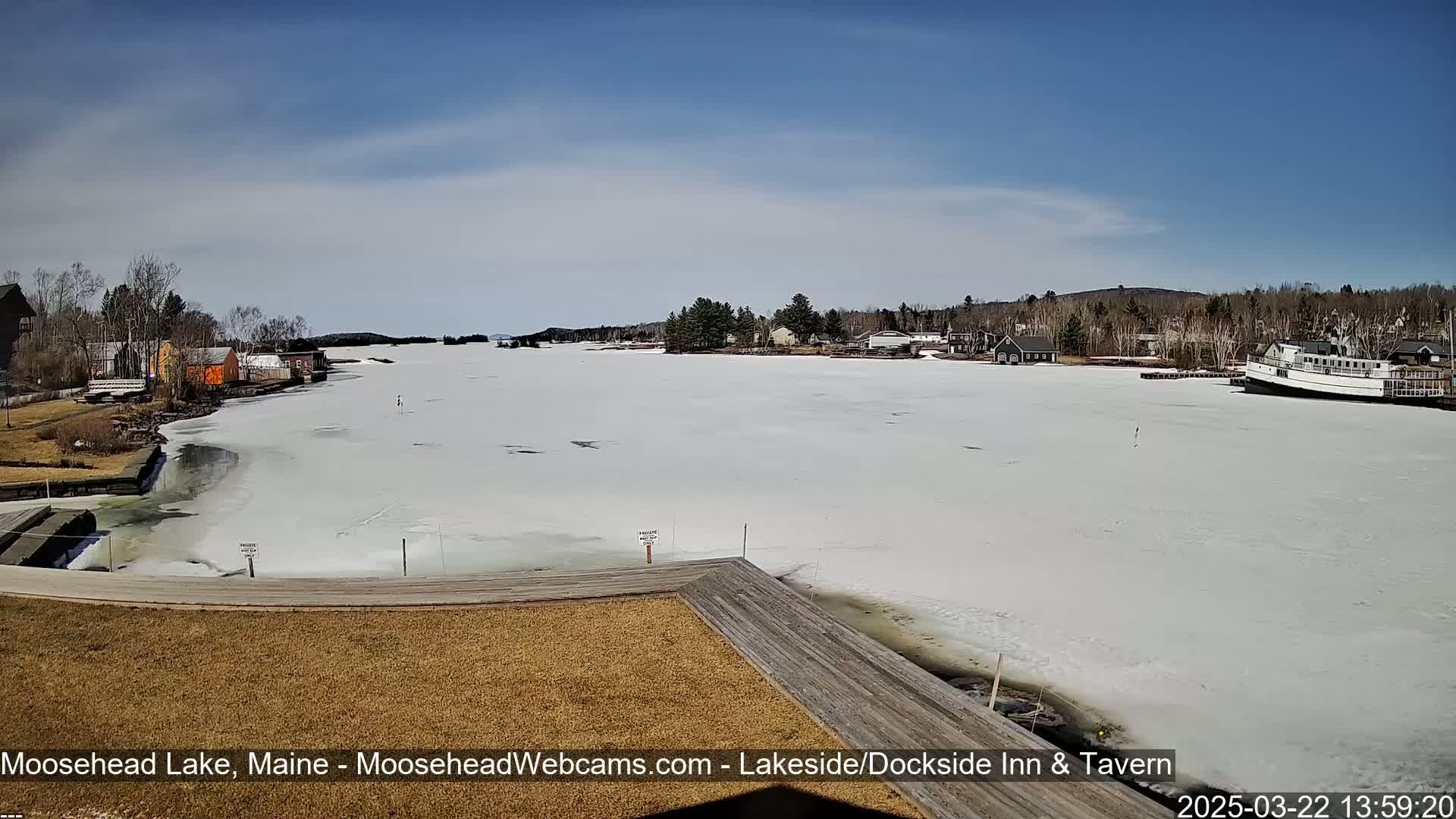 A mostly frozen lake is seen from a lakeside dock, under a partly sunny sky.