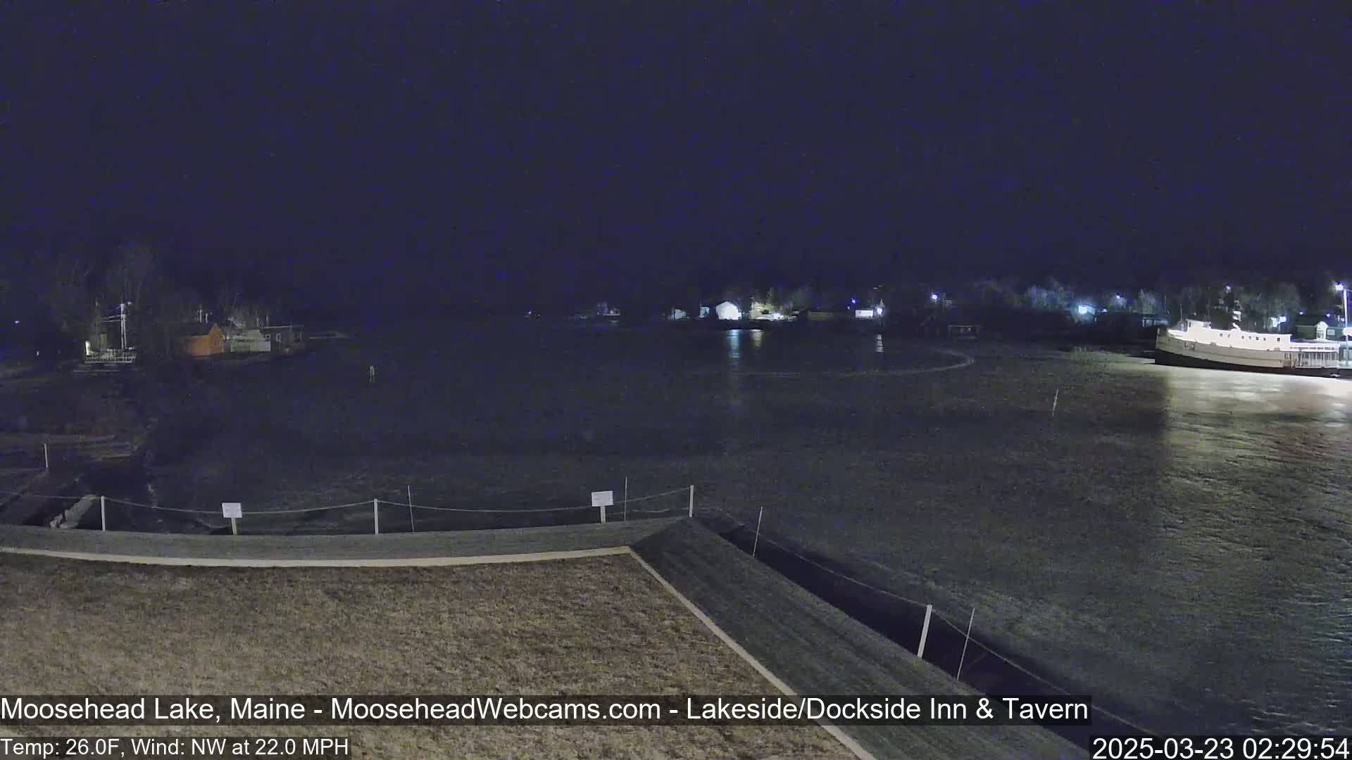 A nighttime view of a lake with a boat docked, buildings on the shore, and a windy, cold (26°F) northwest wind.