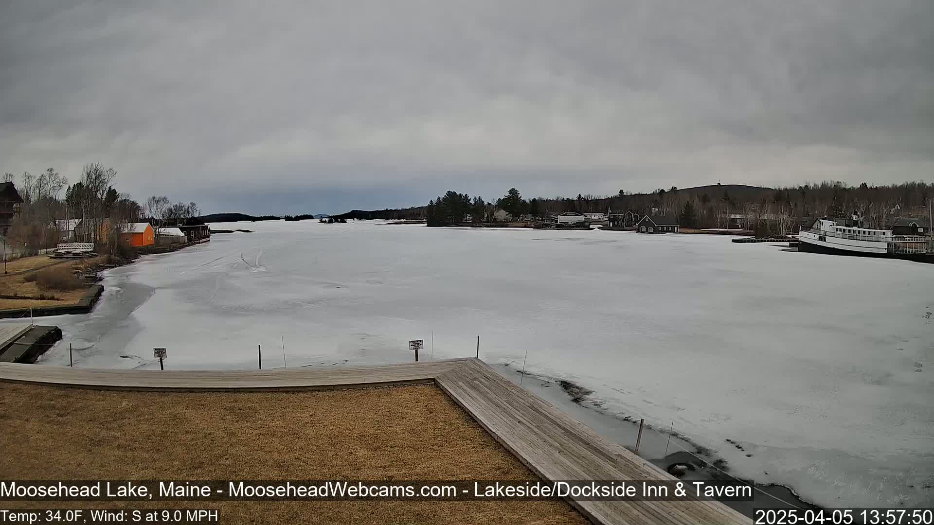 A partially frozen lake is seen from a lakeside dock, under an overcast sky.