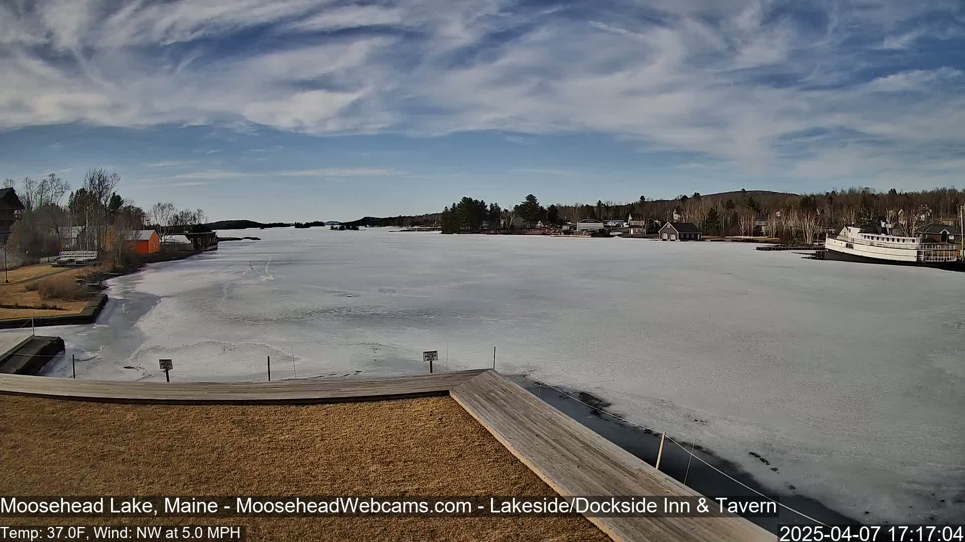 A partially frozen lake is seen from a dock on a partly cloudy day with a light northwest wind.