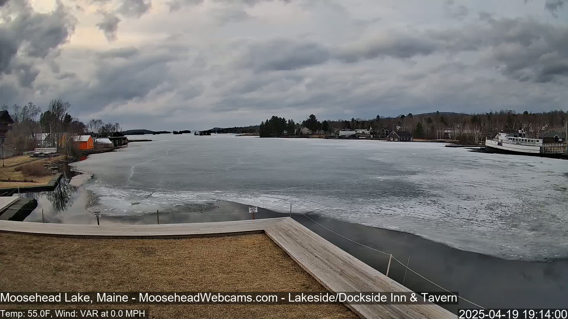 A partly frozen lake is viewed from a wooden dock under an overcast sky.