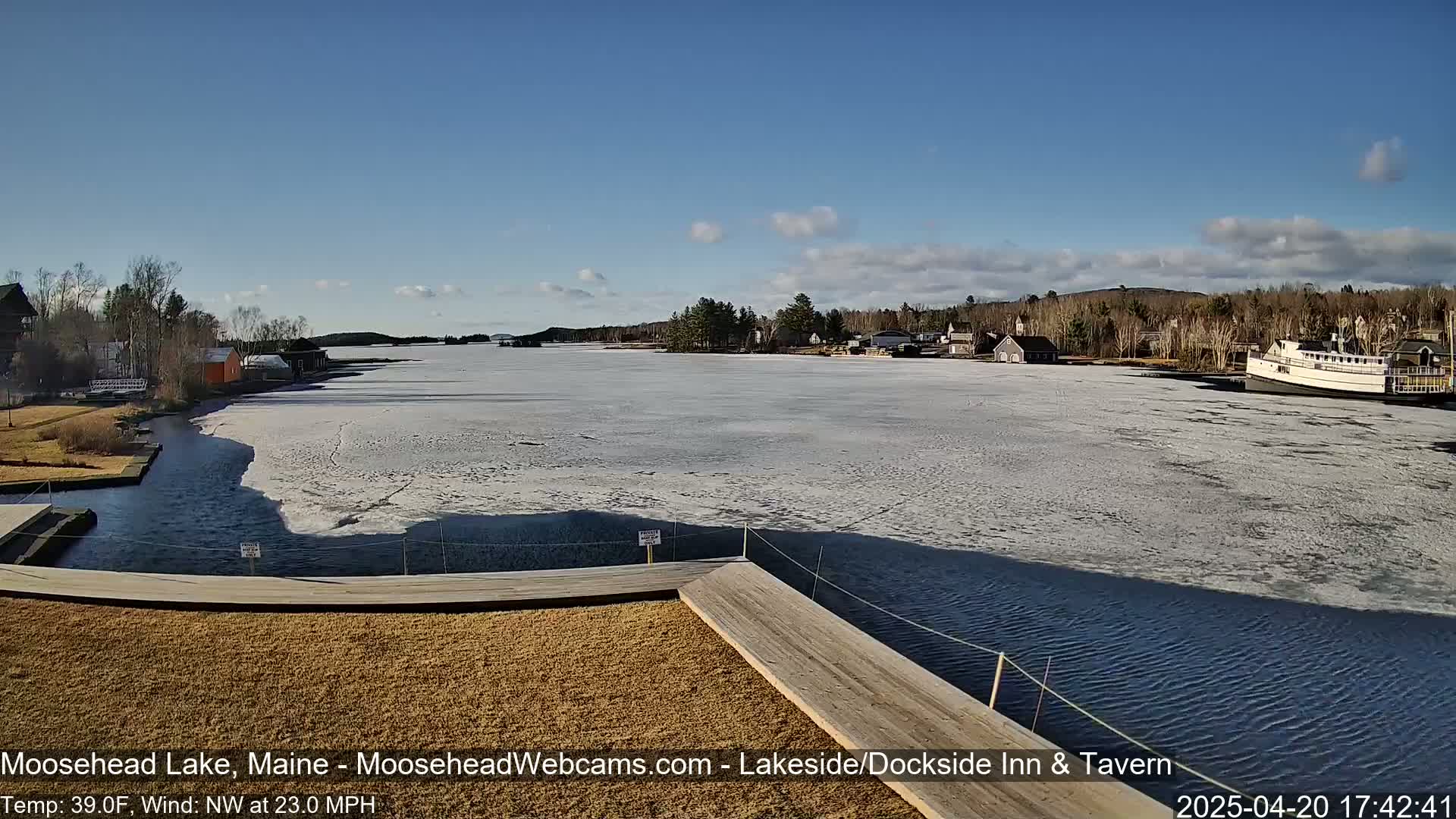 A partially frozen lake is seen from a wooden dock on a sunny day with a northwest wind.
