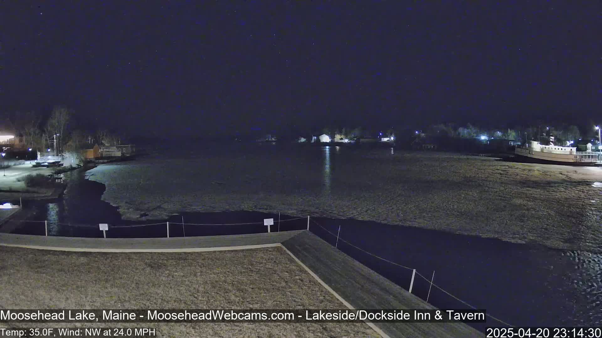 A nighttime view of a partially frozen lake under a starry sky with a 24 mph northwest wind and a temperature of 35°F.
