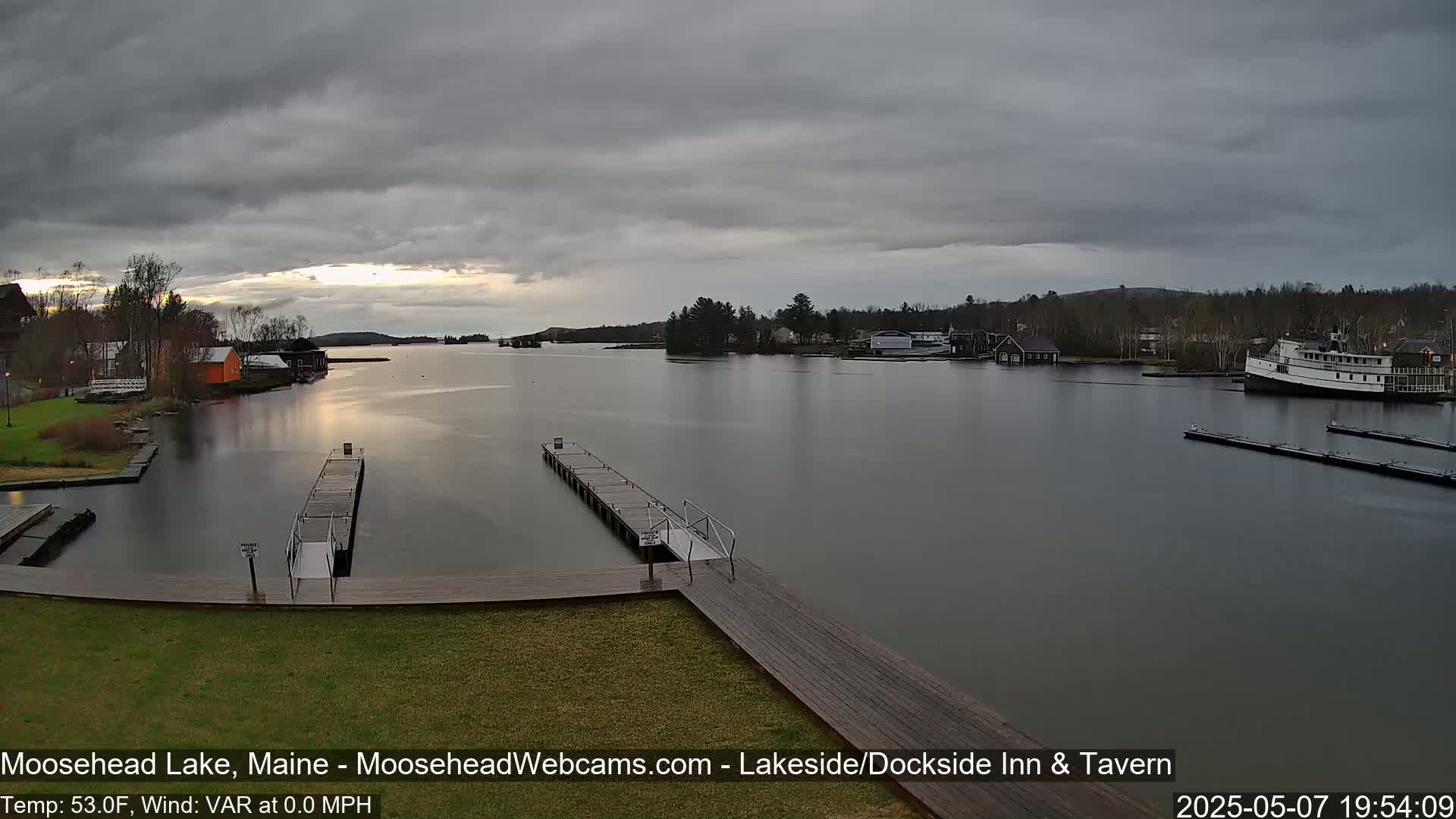 A calm lake with overcast skies, docks, and buildings along its shores, a boat moored near the shore.