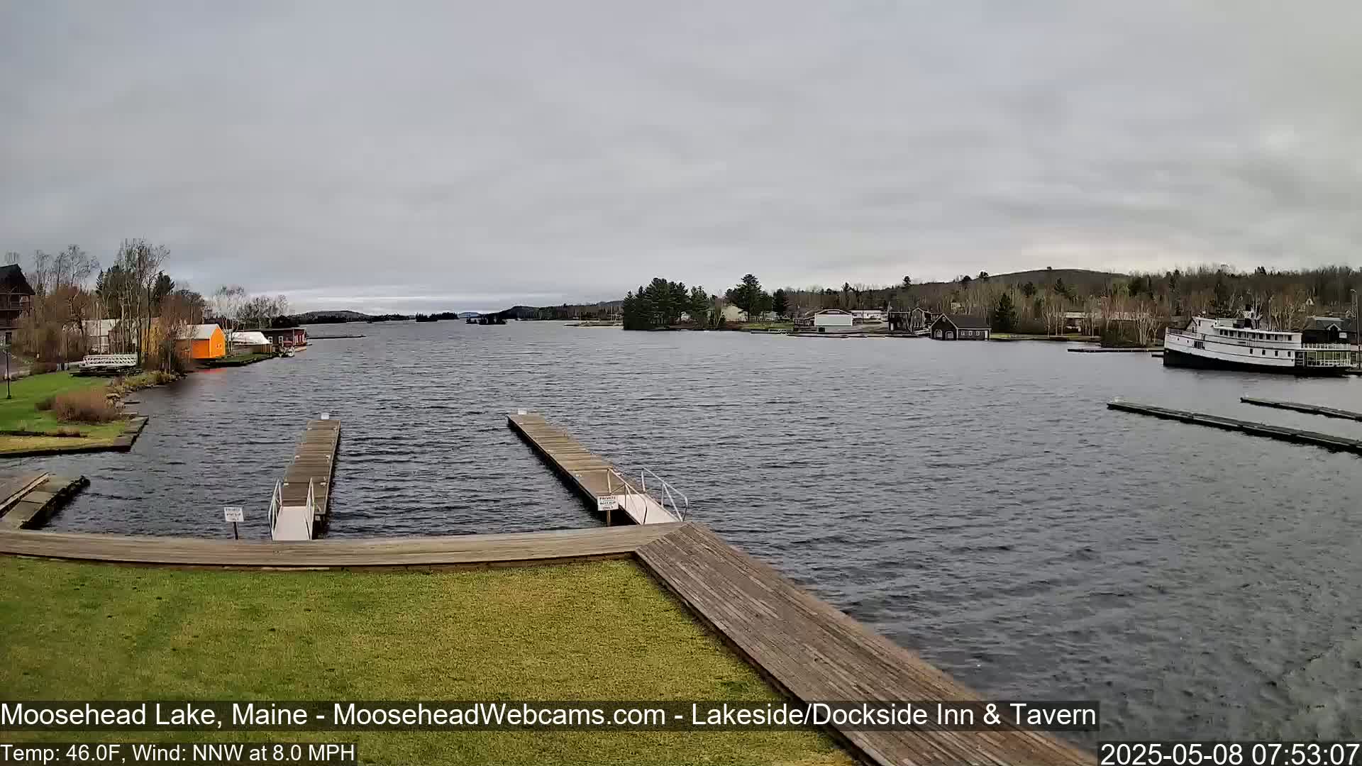A calm lake with several docks and a large boat is seen under an overcast sky.