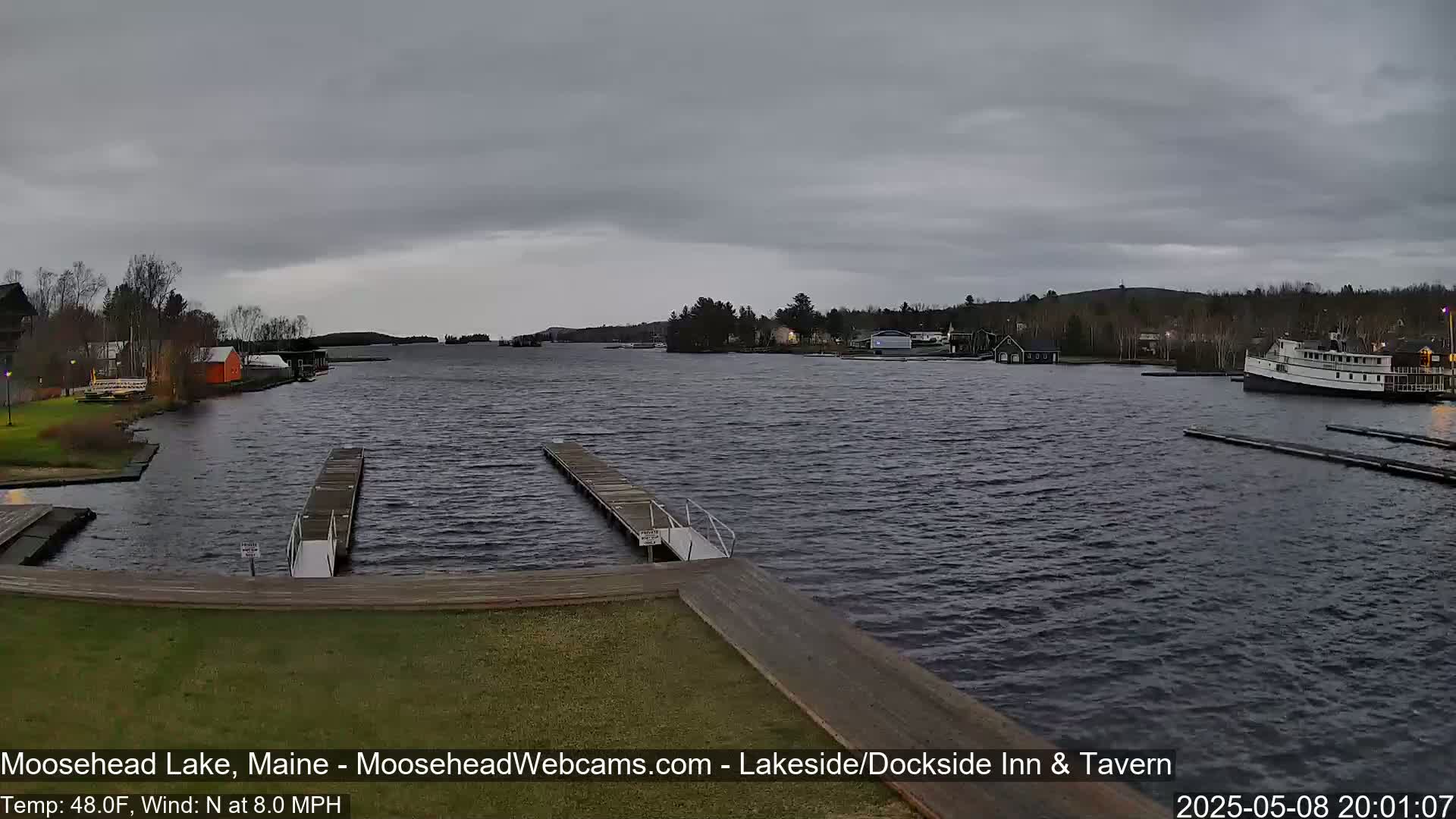 A lake with docks and a boat is visible under an overcast sky, with a moderate north wind.