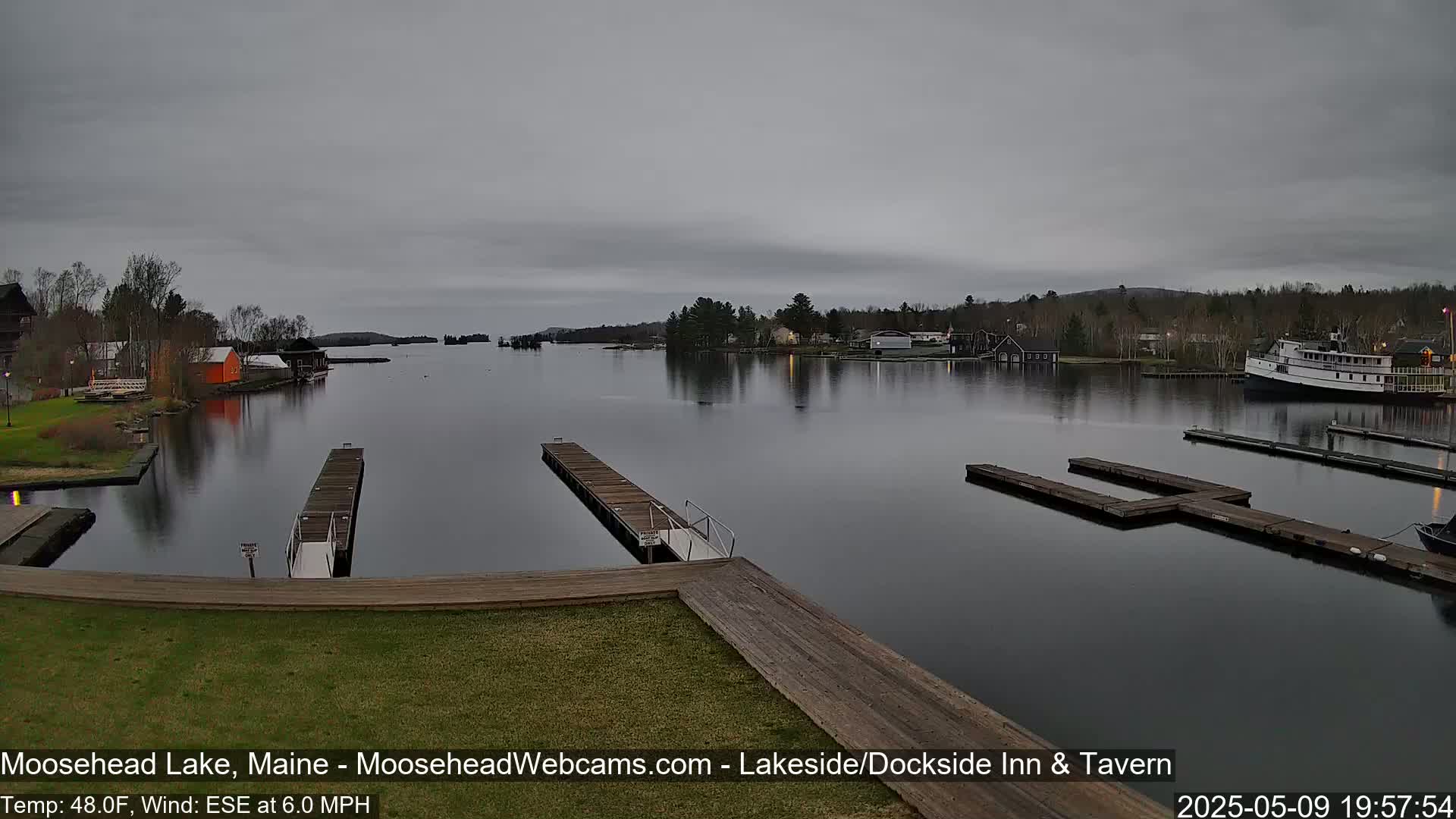 A calm lake with several docks and buildings along its shore under an overcast sky.