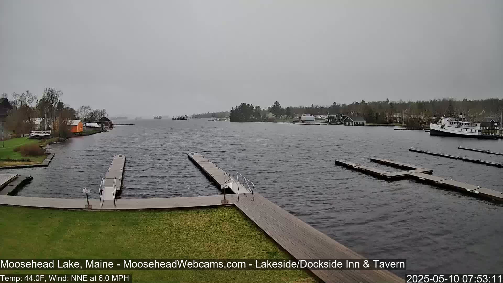A calm lake with several docks and a large boat is seen on an overcast day.