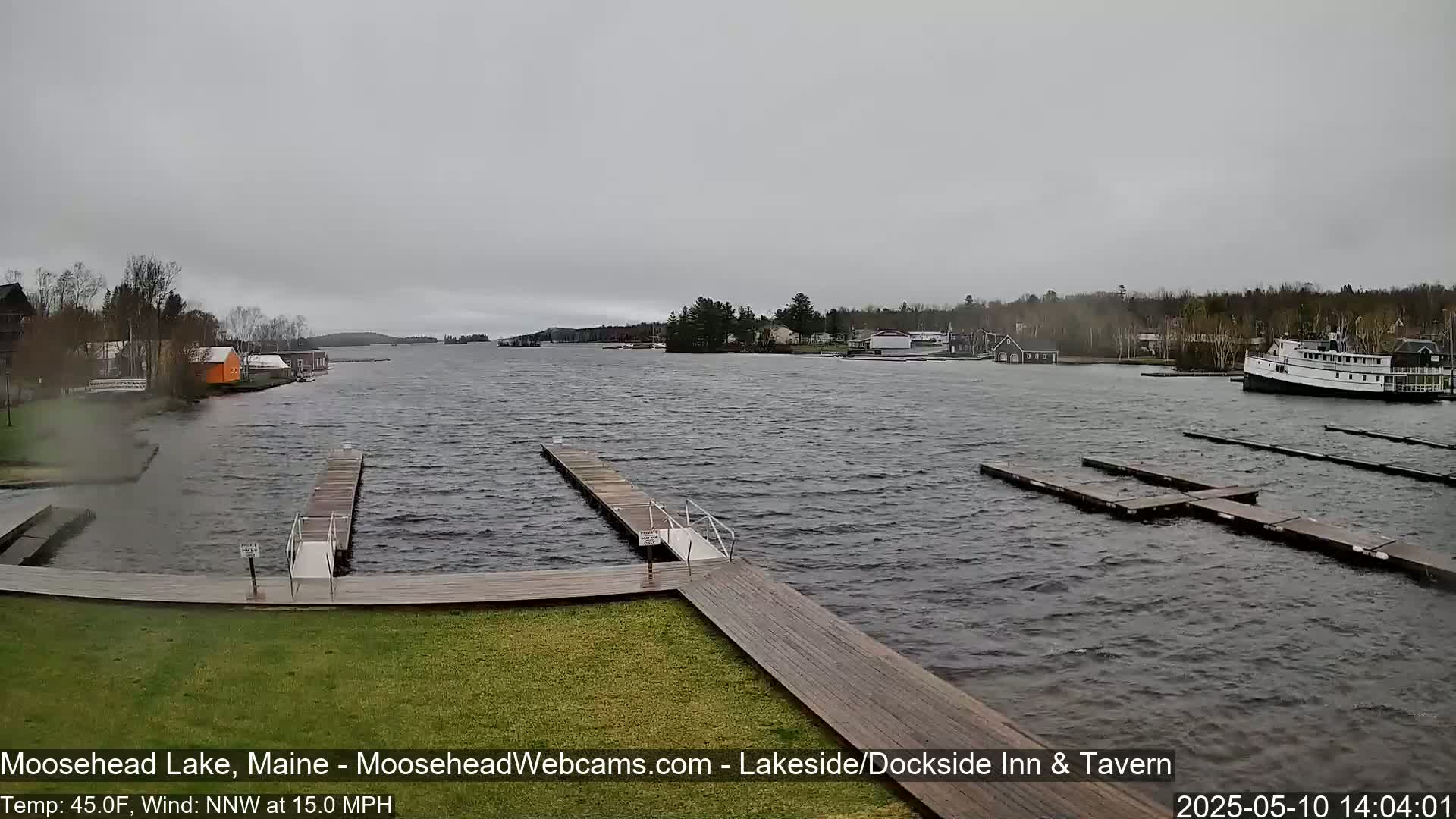 A gray, overcast day shows a lake with several docks, a large boat, and buildings along the shoreline.