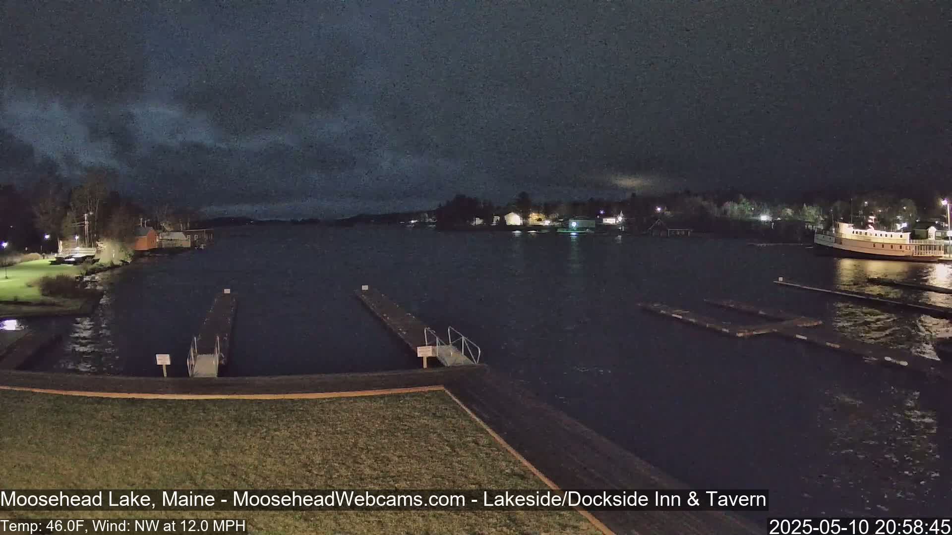 A nighttime view of a lake with docks and a boat, under a partly cloudy sky, with a moderate northwest wind.