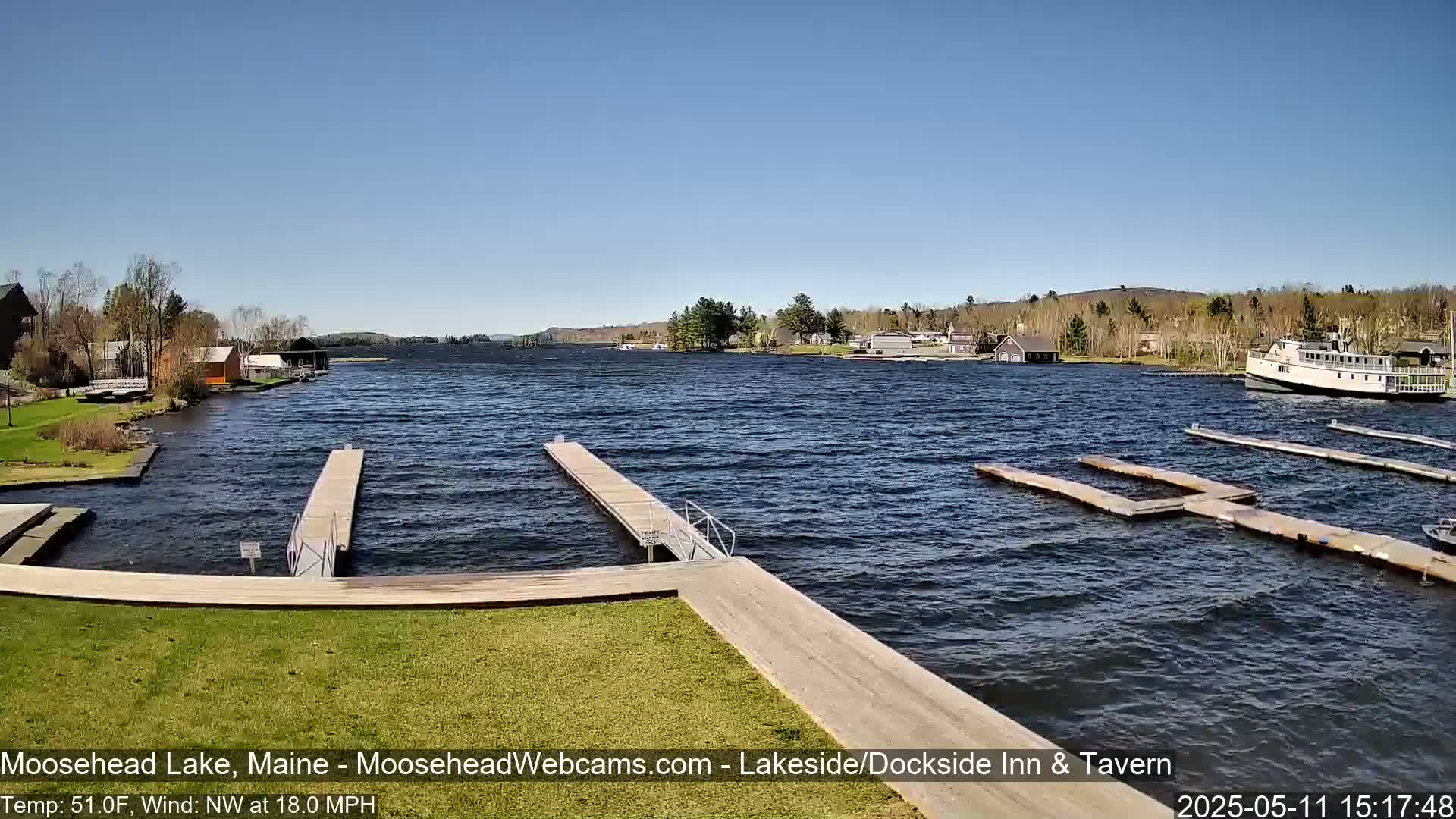 A partly sunny day with a northwest wind shows a lake with several docks and a boat, with green grass and trees in the background.
