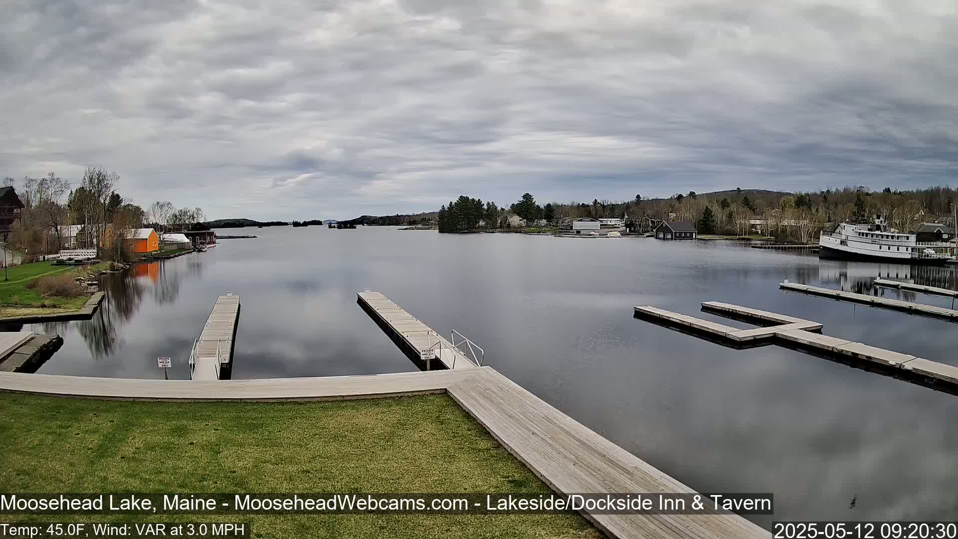 A calm lake with several docks and buildings on the shore under a cloudy sky.